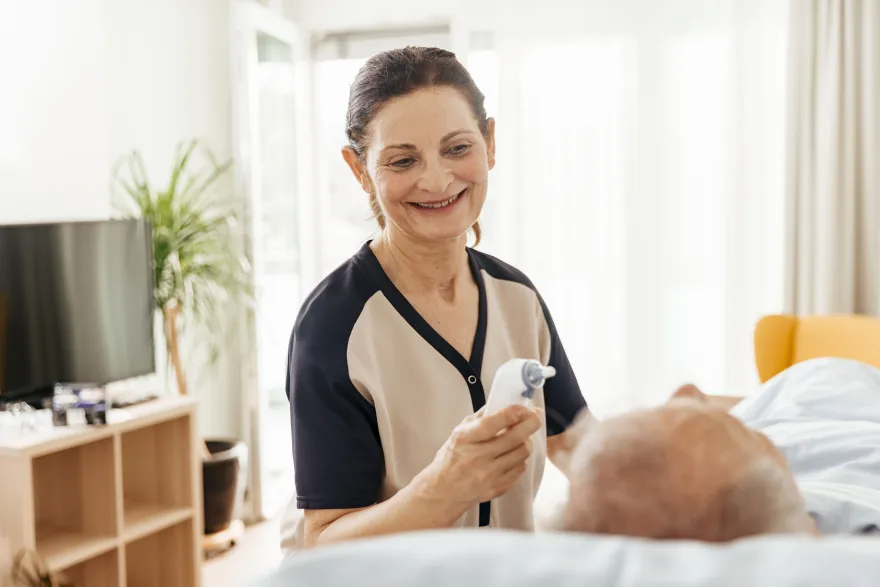 Pflegehelfende SRK beim Fiebermessen bei einem älteren Herrn.